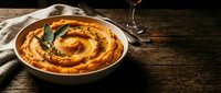 Golden baked pumpkin pie with decorative swirl pattern and sage leaves on rustic wooden table with wine glass, autumn dessert for holiday celebrations.