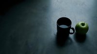 Black mug and green apple on dark textured surface, minimalist still life composition for beverage, food, and lifestyle design projects.
