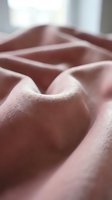 Soft pink fabric with gentle folds and creases creating elegant textile waves. Cozy material texture for home decor and fashion design projects.