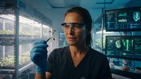 Female scientist in protective eyewear examining test tube in modern laboratory with digital displays and medical equipment for research analysis.