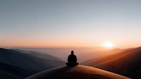 Person meditating on mountain peak during golden hour sunrise with layered hills and warm atmospheric light for wellness and mindfulness concepts.