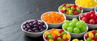 Colorful assorted candies and sweets in white bowls on dark wooden surface for party treats, dessert buffet, confectionery display and celebration snacks.