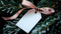 Blank white gift tag with pink satin ribbon bow attached to fresh pine branches with frost and snow detail, creating festive holiday atmosphere.