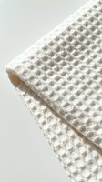 Folded white waffle weave textile with detailed honeycomb texture, soft natural cotton fabric close-up on light background for home decor.