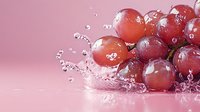 Fresh red grapes with water splash and droplets on pink background, macro photography showing juicy fruit texture in dynamic composition.