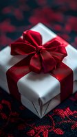 Elegant white gift box wrapped with luxurious red satin ribbon bow on dark background with red floral pattern. Close-up macro photography with selective focus.