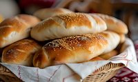 Fresh baked bread rolls with sesame seeds in wicker basket, golden brown crust, soft homemade buns on checkered cloth, close up view of bakery goods.
