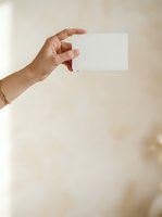 Female hand with medium skin tone holding blank white card against neutral beige background, suitable for business cards, gift cards, promotional materials, and marketing campaigns.