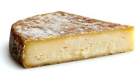 Wedge of aged artisanal cheese with natural rind showing crystallization and creamy pale yellow interior on white background, isolated food photography for culinary use.