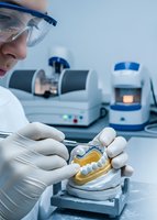 Female dental technician working with dental prosthetics in modern laboratory with professional equipment and safety glasses for precision work.