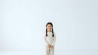 Young Asian girl with long braided hair wearing cream-colored sweater standing against white background, suitable for educational materials, children's content, and family-oriented design projects.