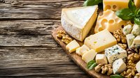 Assorted cheese platter with brie, blue cheese, swiss and nuts on rustic wooden board garnished with fresh herbs, close up view for gourmet food styling.