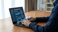 Professional businessman analyzing financial data and charts on laptop computer at wooden desk in modern office environment for business analytics and reporting.