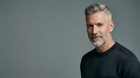 Middle-aged man with gray hair and beard wearing dark charcoal sweater against neutral gray background for corporate, business, and professional portrait use.