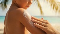 Woman applying sunscreen lotion on shoulder at tropical beach with ocean and palm trees, sun protection skincare routine.