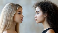 Side profile portrait of two diverse young women facing each other - blonde Caucasian and African American with curly hair, representing unity and racial harmony in modern society.