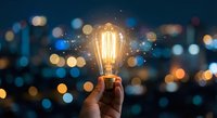 Hand holding glowing vintage Edison bulb against blurred city lights at night. Innovation, creativity and bright ideas concept for business and technology.