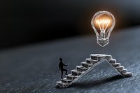 Small silhouette figure climbing stairs toward glowing lightbulb, representing business success, innovation and achievement concept on dark background.