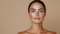 Young Mediterranean woman with natural makeup, glowing skin, and sleek dark hair in center part poses against neutral beige background for beauty and skincare advertising.