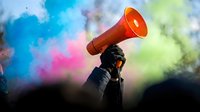 Person with red megaphone speaking against vibrant colorful smoke background for protest rally communication and activism campaigns.