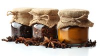 Glass jars with honey and coffee beans wrapped in burlap cloth, decorated with star anise and spices on white background, food photography styling.