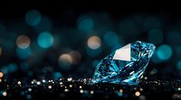 Blue diamond on dark background with bokeh lights and reflections creates luxurious gemstone composition for jewelry advertising and luxury concepts.