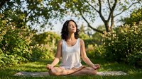 Young woman practicing yoga meditation outdoors in peaceful garden setting during golden hour sunlight for wellness and mindfulness lifestyle.