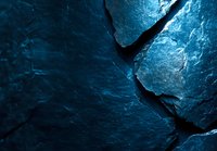Dark blue cracked stone surface with dramatic lighting creates abstract pattern and deep shadows, showcasing natural texture and geological formations.