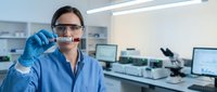 Female scientist in blue lab coat examining test tube sample in modern laboratory for medical research and analysis.