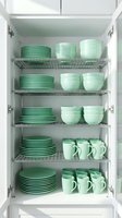 Organized kitchen cabinet with green ceramic dinnerware set including plates, bowls and mugs on wire shelves for home storage and organization.