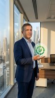 Confident middle-aged Caucasian businessman in navy suit holding glowing green sustainability symbol in modern office with city skyline view for corporate responsibility.