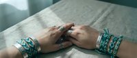 Woman hands with turquoise silver jewelry bracelets and rings resting on white bedding in soft natural light for fashion accessories styling.