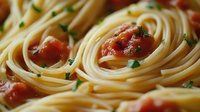 Fresh spaghetti pasta with cherry tomatoes and chopped herbs in tomato sauce, close-up macro food photography showing texture and ingredients.