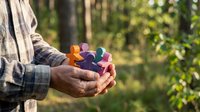 Senior man hands holding colorful puzzle pieces outdoors representing teamwork, problem solving and mental health awareness in natural setting.