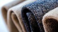 Macro view of folded denim and textile fabrics showing detailed weave pattern and texture in blue and beige tones, selective focus creates artistic depth.