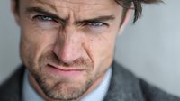 Middle-aged Caucasian businessman with intense angry expression and furrowed brow showing frustration and displeasure in professional corporate setting.