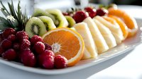Fresh fruit platter with sliced orange, kiwi, pineapple and raspberries arranged on white plate for healthy breakfast, catering or party appetizer.