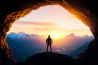 Silhouette of adventurous hiker standing at cave entrance overlooking majestic mountain range and winding river valley during golden sunset with dramatic sky.