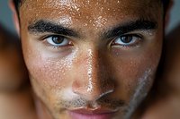 Close up portrait of young Latino male model with intense blue eyes, glowing sweaty skin, and strong facial features against dark background. Artistic beauty concept.