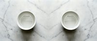 Two empty white ceramic bowls placed symmetrically on elegant marble surface with natural veining patterns for kitchen dining and food presentation concepts.