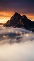 Dramatic mountain peak emerging from clouds at golden hour sunrise with warm orange and purple sky creating majestic alpine landscape for nature photography.