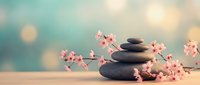 Zen spa stones balanced with delicate pink cherry blossom branches on wooden surface against soft bokeh background for wellness and meditation concepts.