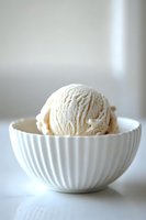 Single scoop of creamy vanilla ice cream served in elegant white ribbed ceramic bowl against soft light background, minimalist food photography styling.