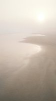 Misty beach shoreline with gentle waves and soft sand dunes in ethereal morning light creating dreamy coastal atmosphere for wellness and travel content.