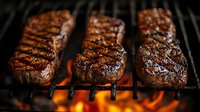 Juicy beef steaks grilling on flaming barbecue grate with fire underneath, showing grill marks and caramelized surface for restaurant menu or cooking concept.
