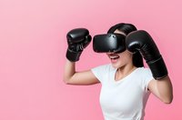 Young Asian woman wearing VR headset and boxing gloves in fighting pose on pink background for fitness technology and virtual reality sports training.