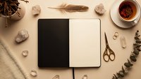 Open notebook with blank pages surrounded by autumn elements, tea cup, scissors, feathers and natural decorations on beige background for creative writing.