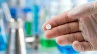 Person holding white pill or tablet in palm with blurred laboratory background, suitable for pharmaceutical, healthcare, medicine, and medical treatment concepts.