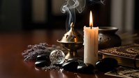 Mystical altar setup with burning candle, crystal ball, incense, black stones and ancient books for spiritual practices, meditation and divination rituals.
