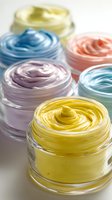 Colorful whipped body butter in glass jars featuring pastel yellow, purple, blue, pink, and turquoise creams for natural skincare products.